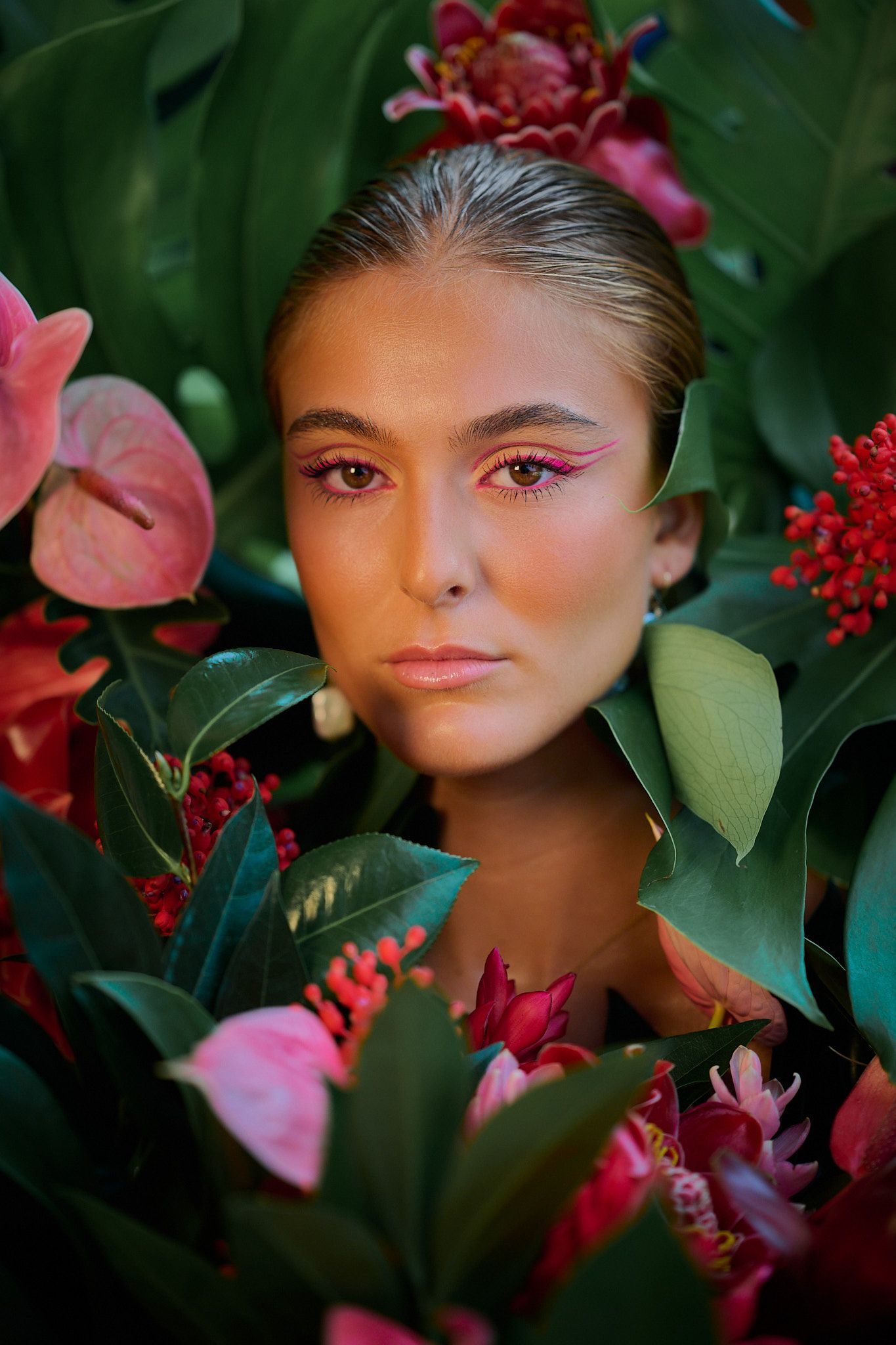 A fashion portrait surrounded by lush green leaves and red berries features vibrant pink makeup artistry.