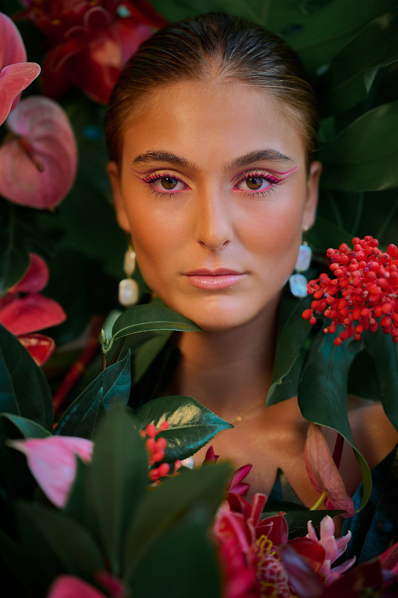 Artistic beauty portrait with pink makeup surrounded by vibrant tropical flowers and red berries in garden setting.