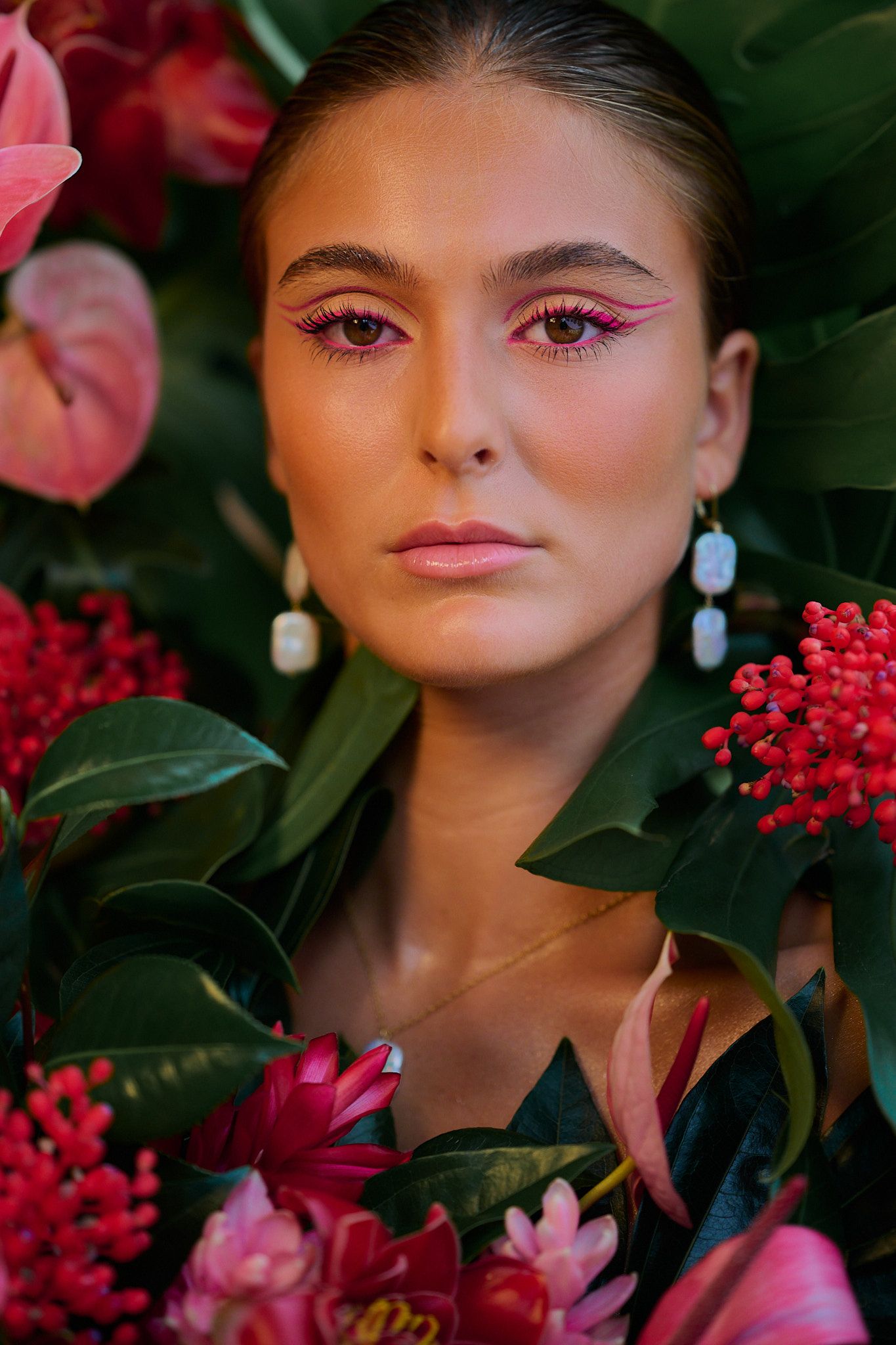 A closeup beauty shot amidst pink flowers and red berries showcases dramatic eye makeup and dangling earrings.