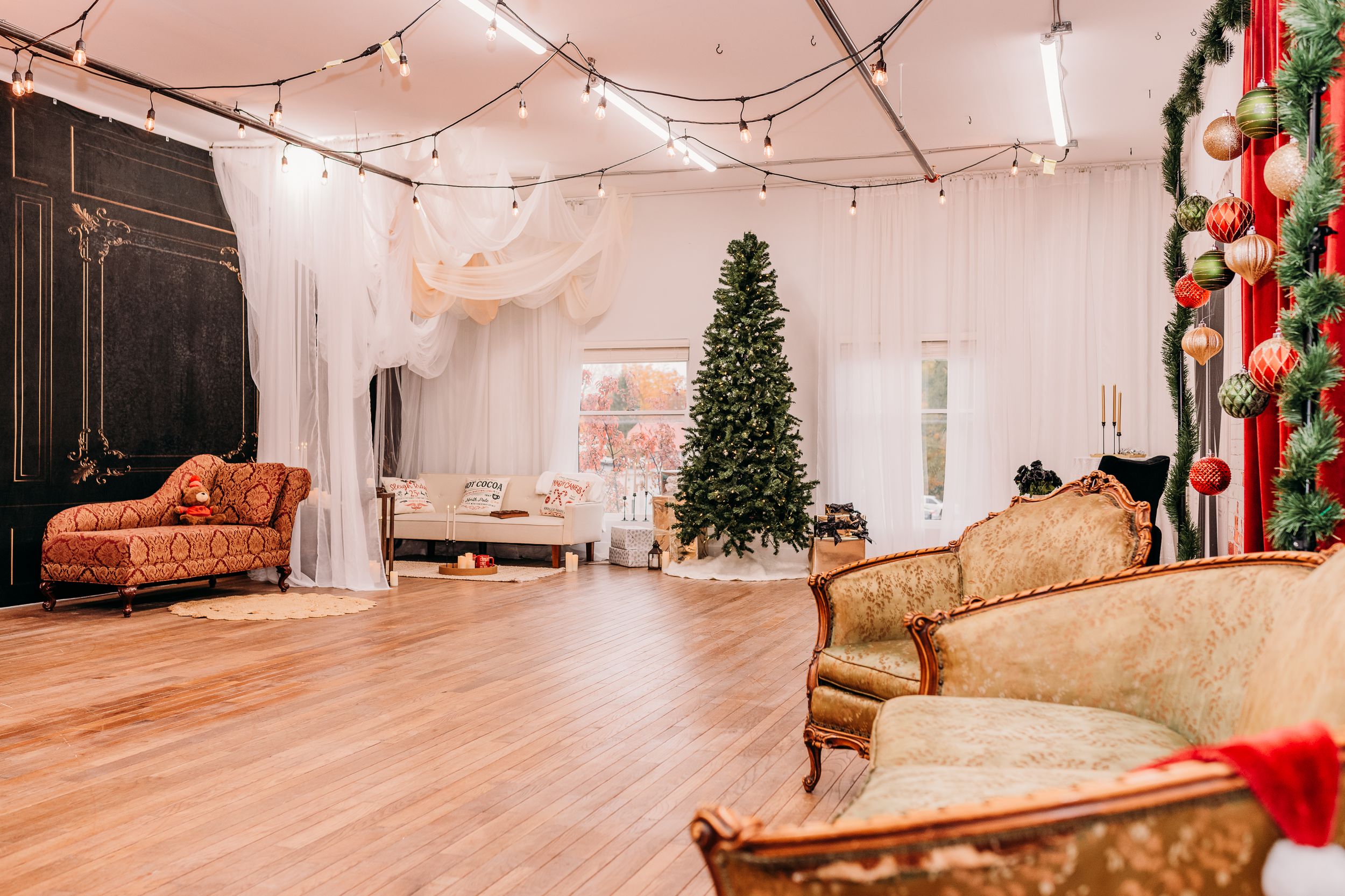 Elegant studio space decorated for Christmas with vintage furniture, string lights, and a tall green tree.