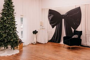 White photo studio interior with large black bow decorations and Christmas trees in corners.
