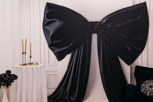 Large black velvet bow decoration mounted on white wall with candlesticks and floral accents in elegant room setting.