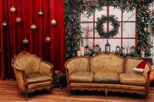 Elegant vintage couch with ornate gold frame against red curtains and festive holiday decorations.