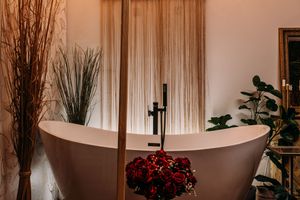 A luxurious spa-like bathroom with freestanding tub, curtains, and decorative branches in a warm-toned setting.