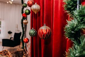 Festive Christmas decorations with red and gold ornaments hanging against red curtains near evergreen branches.