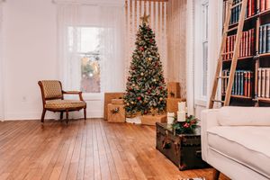A cozy living room decorated for Christmas with a lit tree, vintage armchair, and wooden bookshelves.