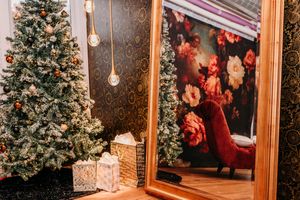 Decorated Christmas tree with wrapped presents next to a gold-framed mirror and glowing pendant lights in a cozy setting.
