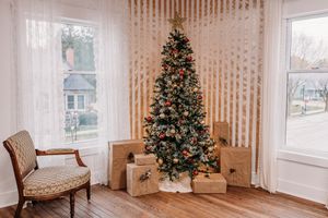 A cozy living room decorated with two Christmas trees and beige vertical striped wallpaper features large windows.