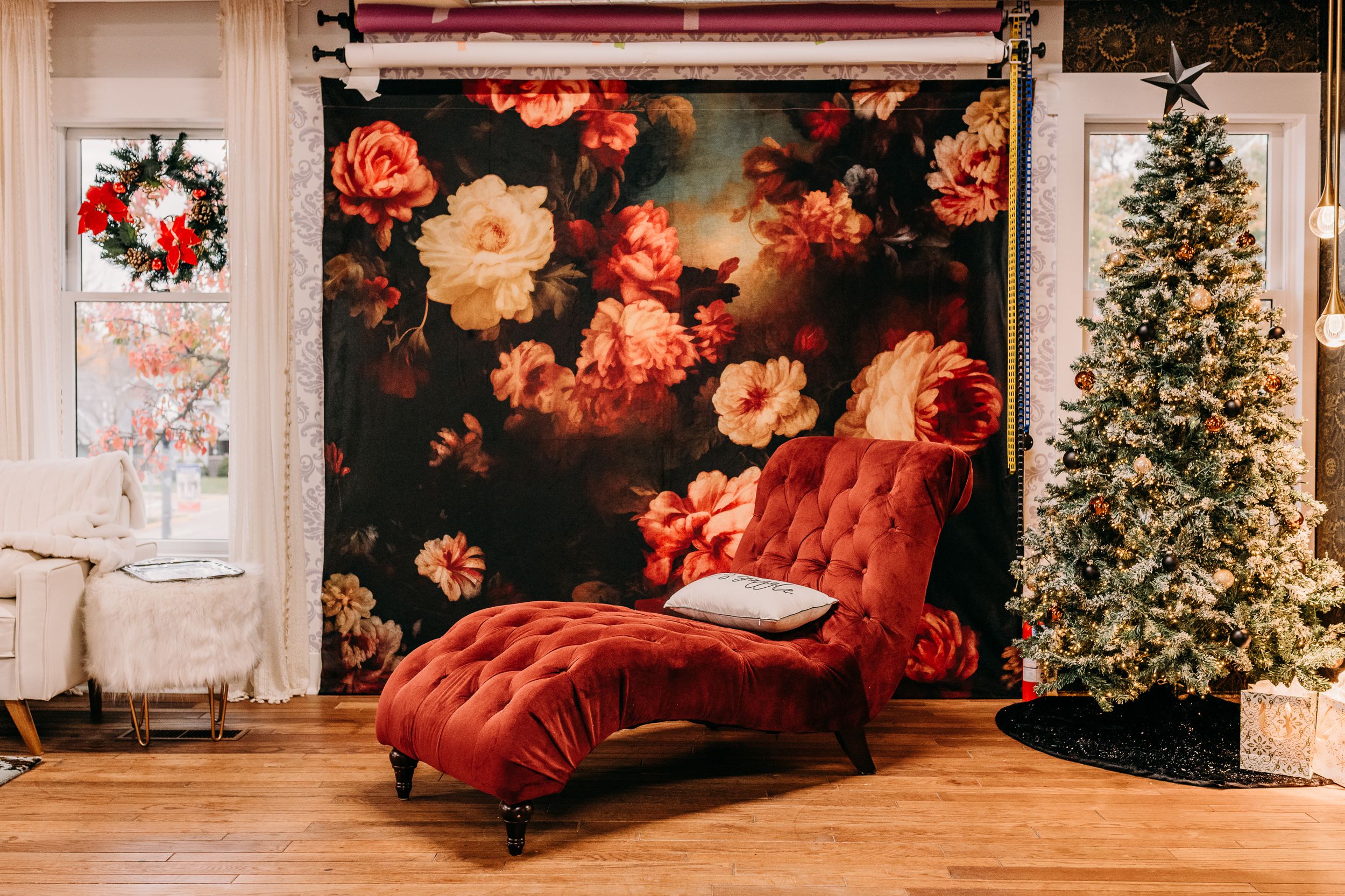 A festive Christmas scene with decorated trees, red velvet chairs, and elegant white walls in a luxurious interior setting.