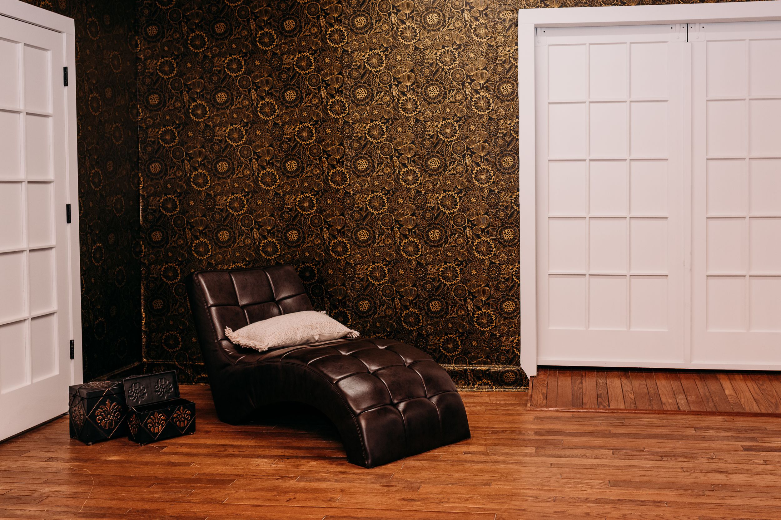A decorative brown wallpaper pattern with floral motifs covers a wall next to white paneled doors and hardwood flooring.
