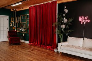 A modern studio space with dark green walls, red curtains, and a neon sign featuring elegant decorative elements. Photography Studio