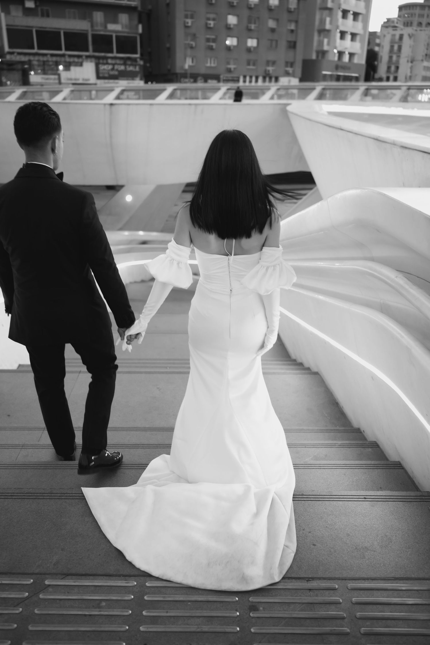 Elegant couple in formal wedding attire walk together outside ornate church entrance with decorative iron gates.