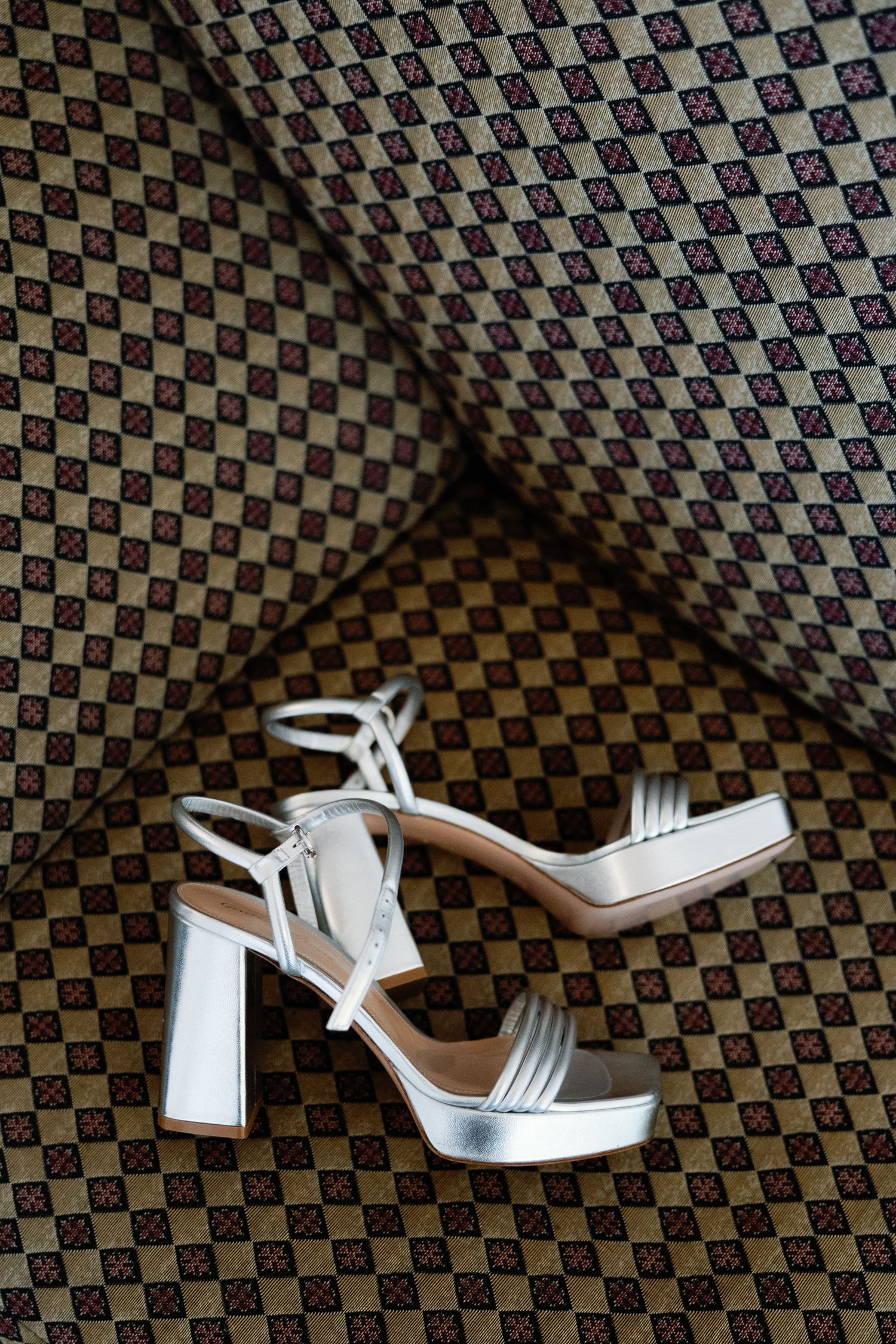 Silver platform wedding sandals with ankle straps displayed on a patterned fabric background.