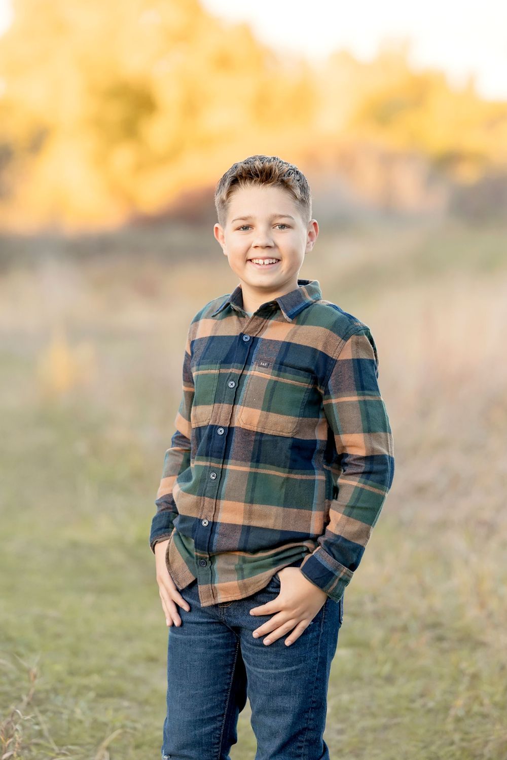 Child wearing plaid flannel shirt poses in golden sunset light. Clear Lake Photographer. Mason City Photographer.