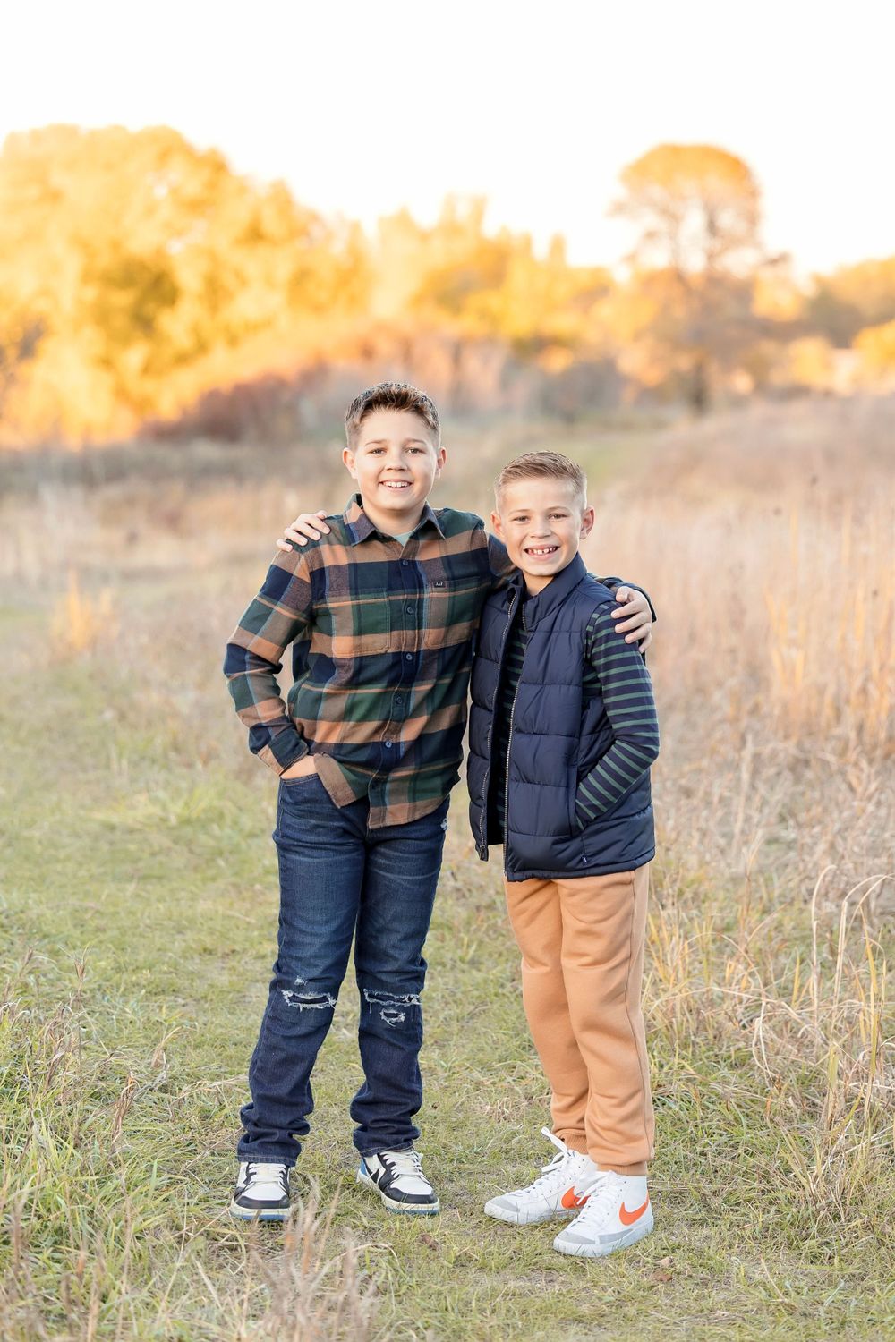 Two children in casual clothing standing together in a sun-lit meadow during fall. Clear Lake Photographer. Mason City Photographer.  Clear