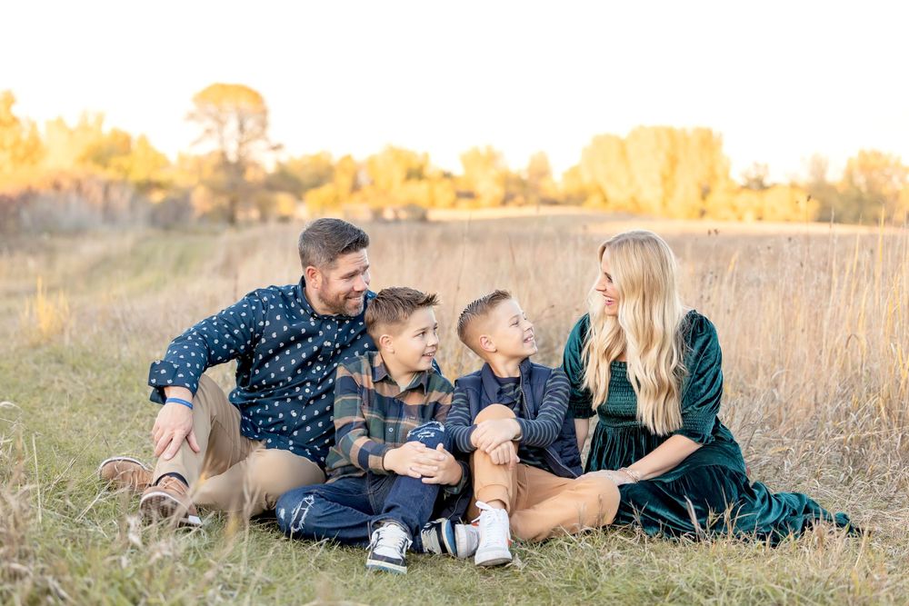 Family lying down together in a grassy field during golden hour. Clear Lake Photographer. Mason City Photographer.