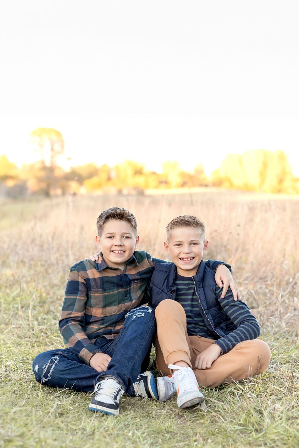 Kids sitting together on grassy ground during an autumn sunset photoshoot.