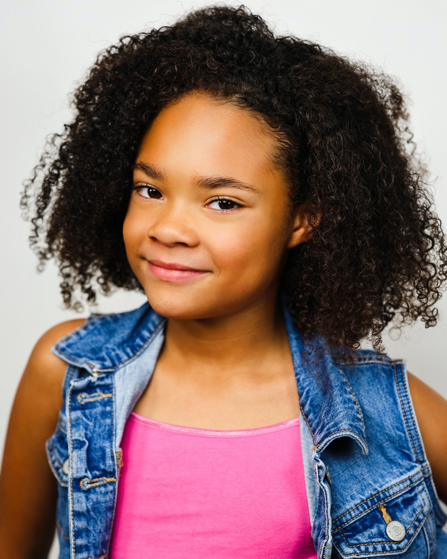 Professional headshot of child model in denim and pink against white backdrop.