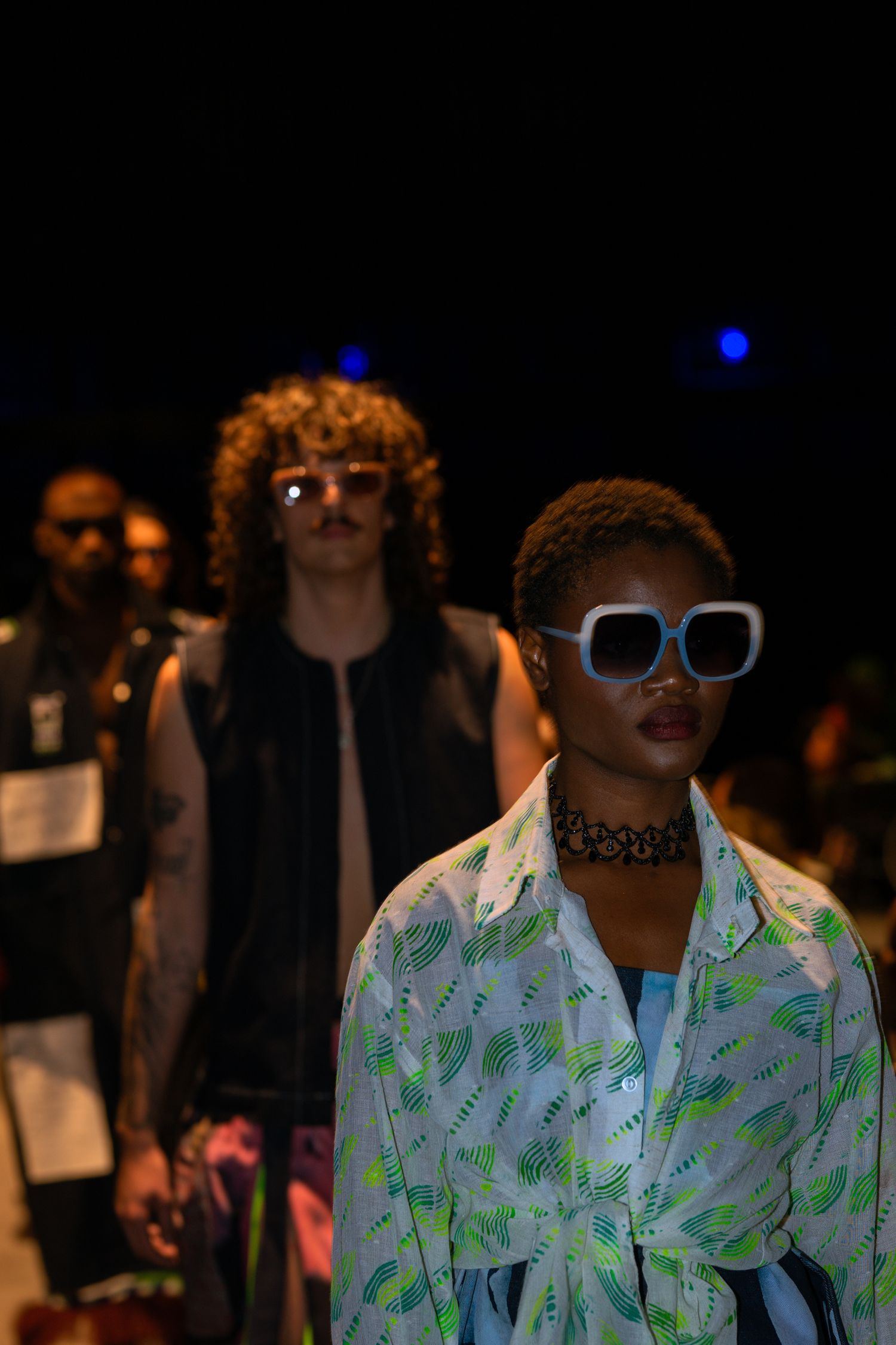 Fashion show attendees in stylish outfits and statement sunglasses.