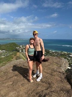 Two hikers posing together on a scenic coastal cliff overlook with ocean views.