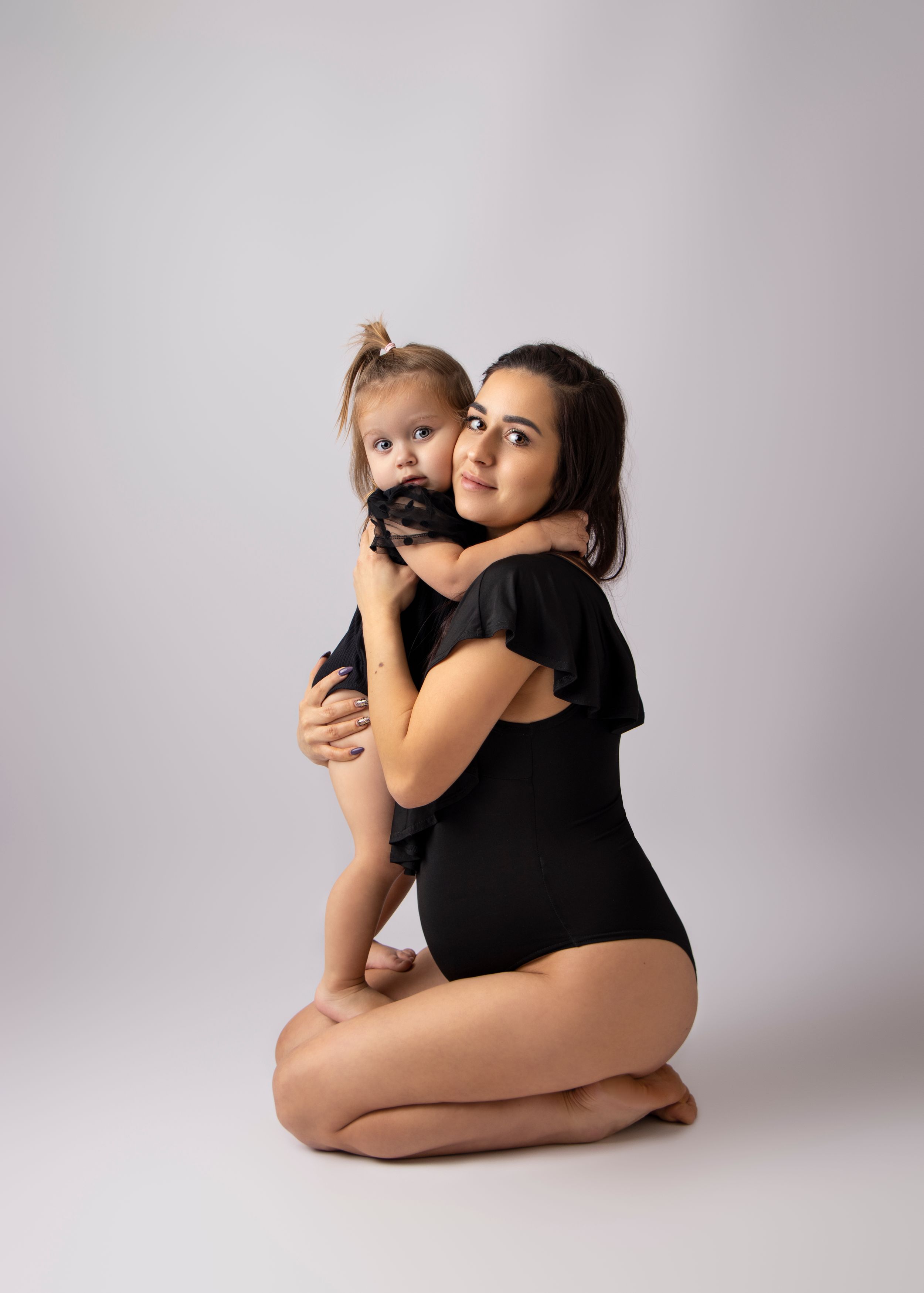A tender embrace between parent and child wearing matching black outfits in studio setting.
