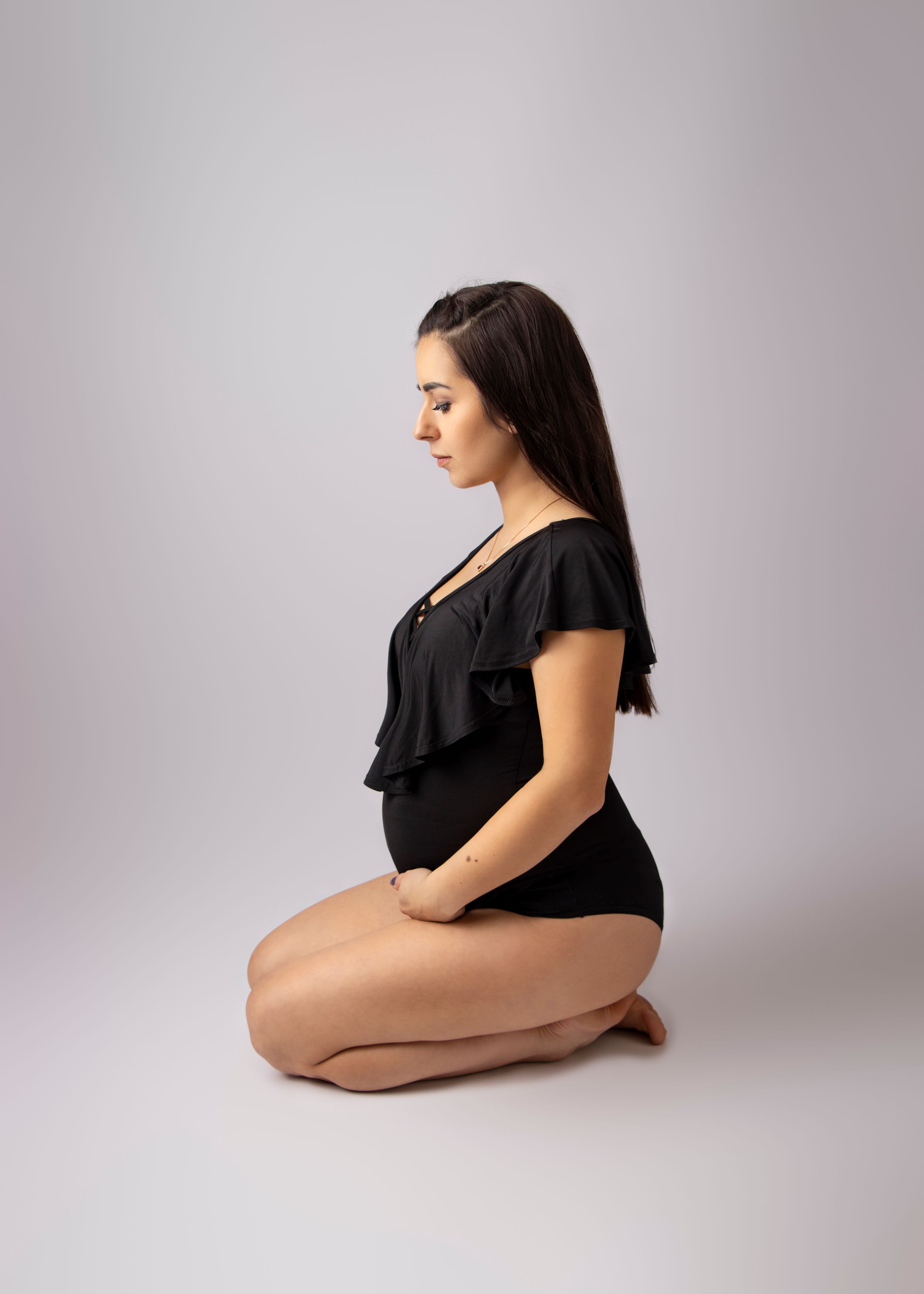 Woman in black bodysuit poses elegantly in profile against neutral background.