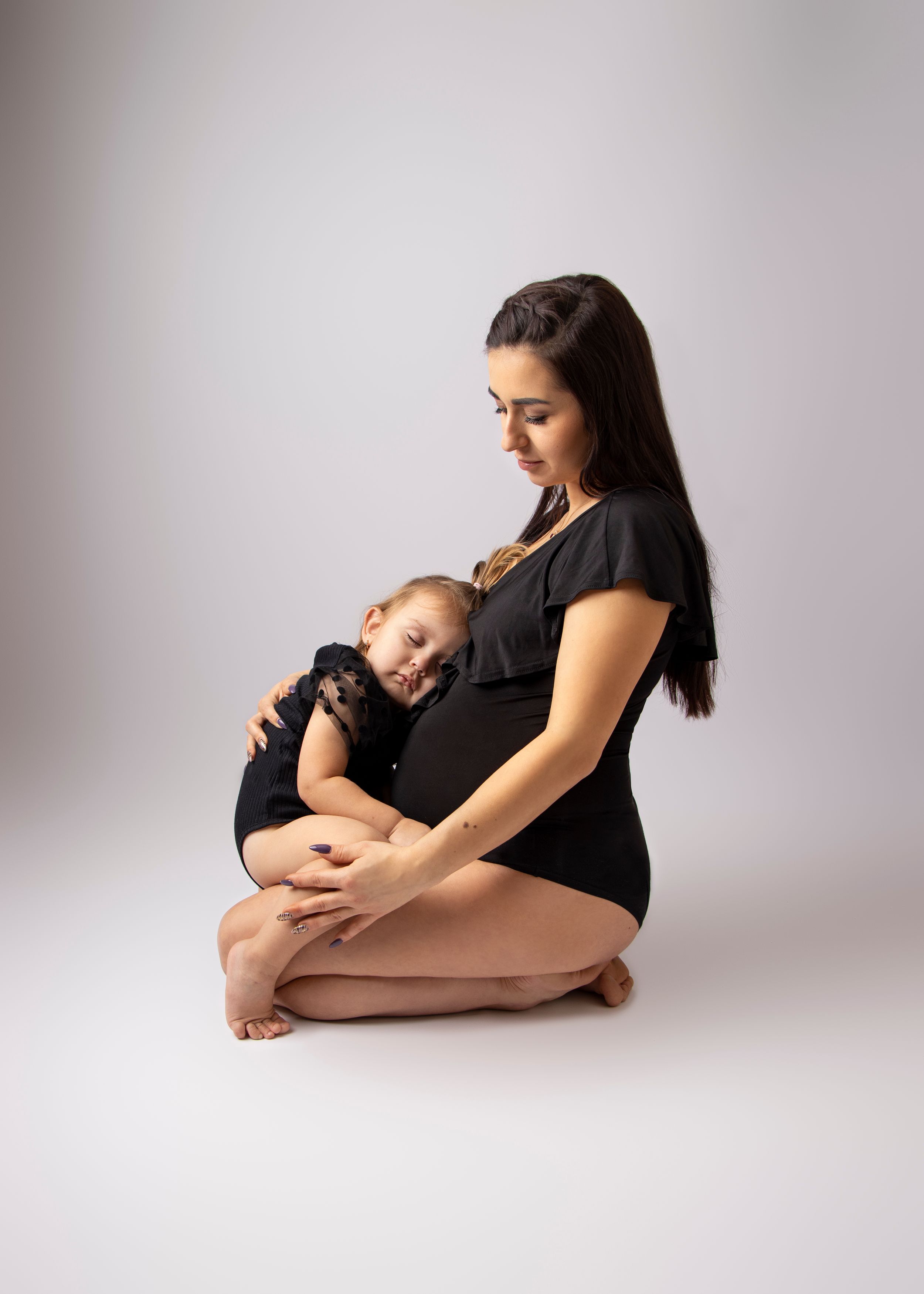 An intimate portrait of a mother and sleeping baby in black attire against a white backdrop.