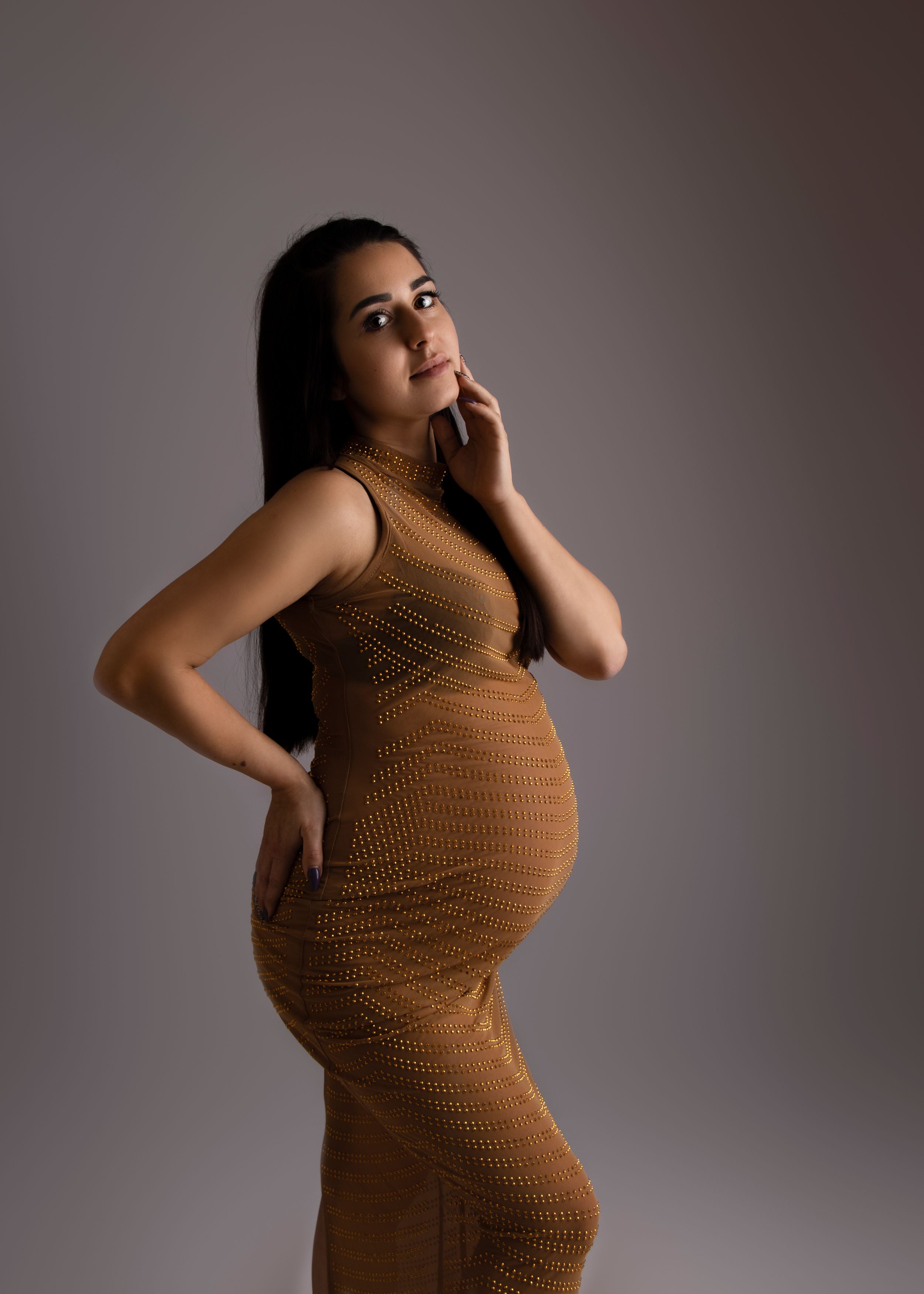 A maternity portrait featuring a form-fitting brown knit dress against a studio backdrop.