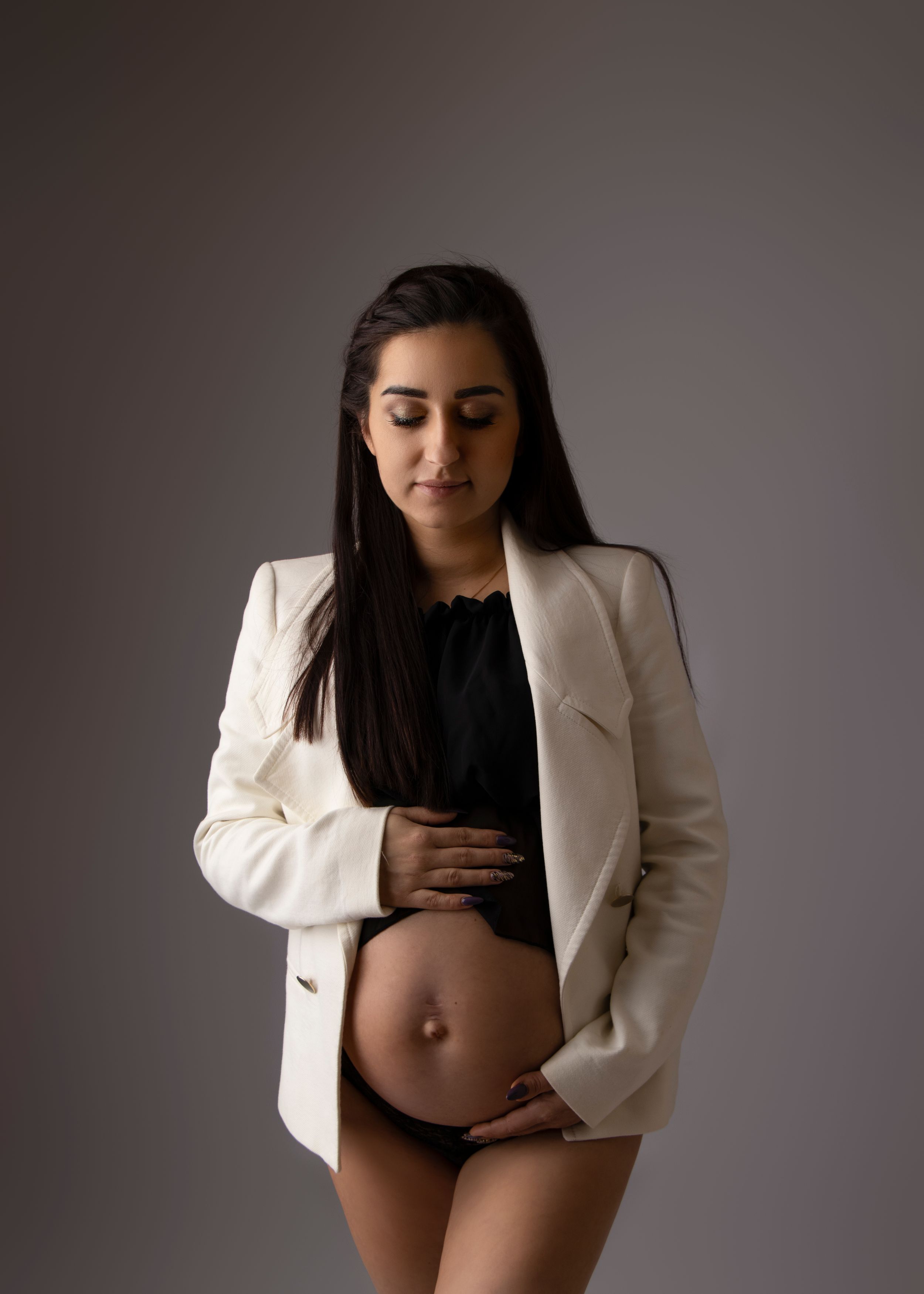 A maternity portrait showing a white blazer and black top against a dark background.