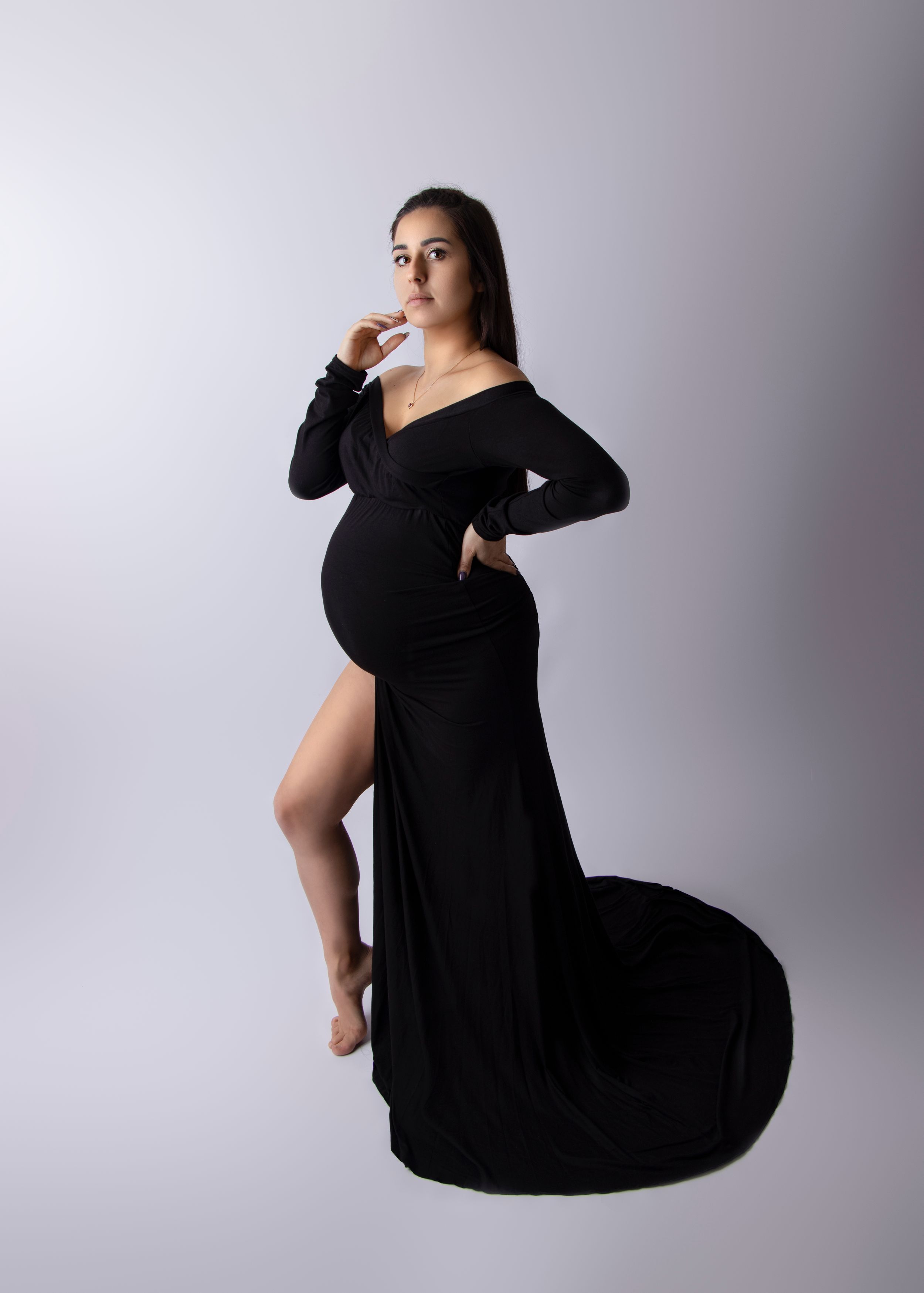 A maternity photo of an expectant mother in a flowing black dress against a light background.