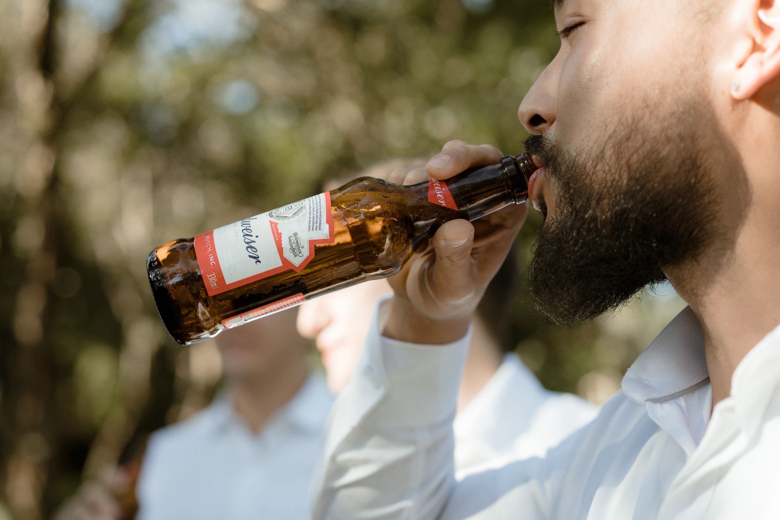Close-up of someone drinking from a beer bottle outdoors.