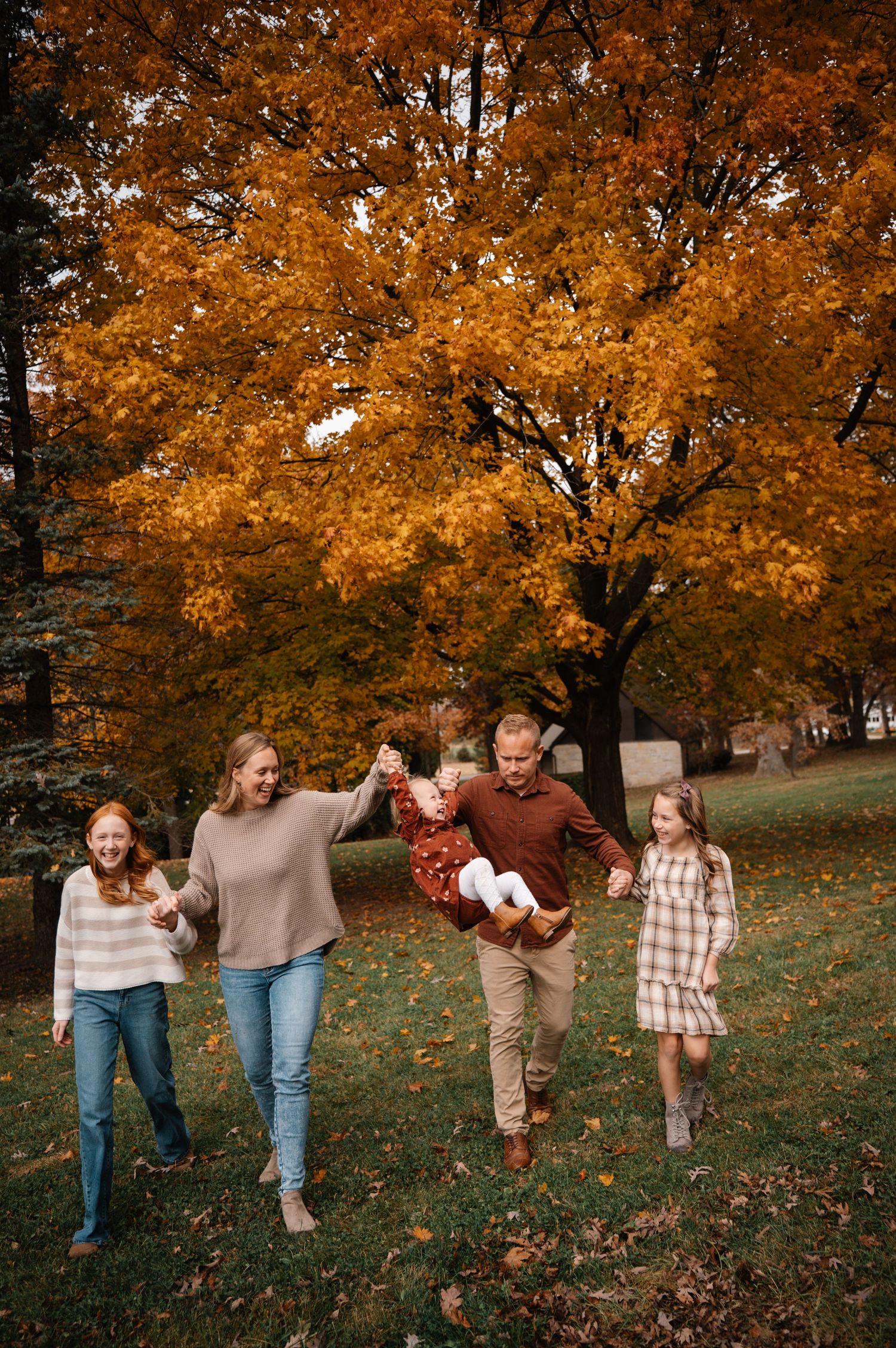 A happy family of five walks through a park beneath a vibrant orange autumn maple tree.