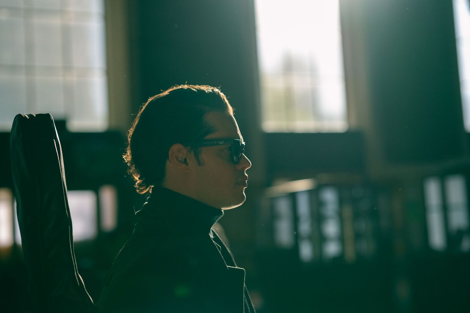 A profile silhouette of a person in sunglasses and turtleneck against a window.