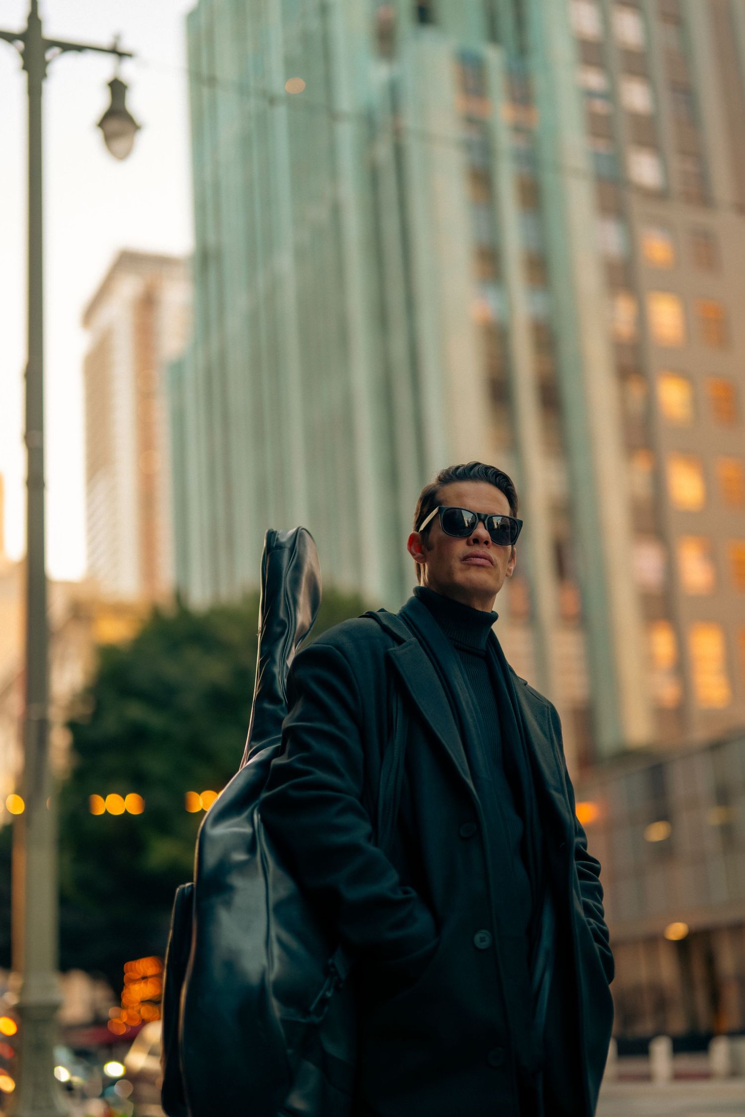 Person in black coat photographed against urban architecture at sunset.