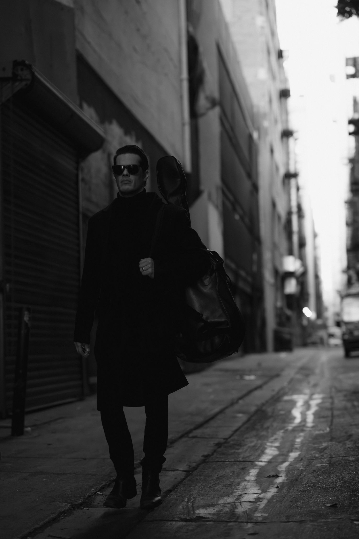 Dramatic black and white photo of figure in dark alley with wet pavement.