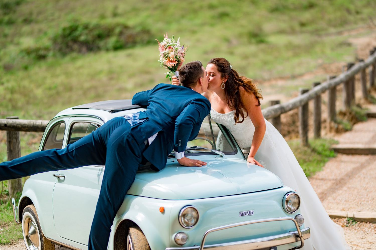 A vintage turquoise convertible car decorated with wedding flowers parked in a sunny garden setting.