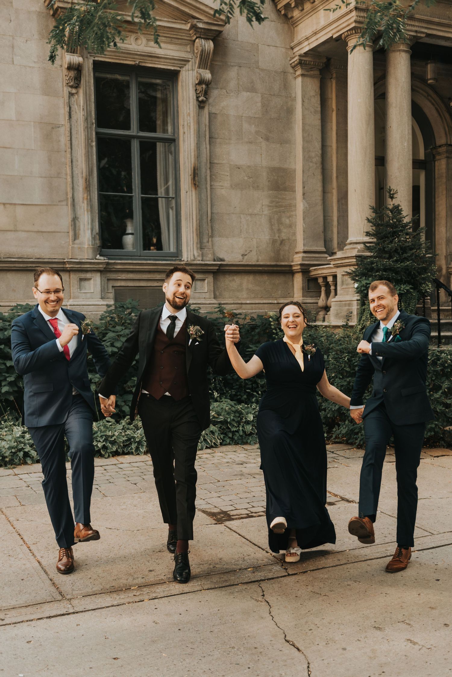 Four people in formal attire walking and laughing together outside a grand historic building with stone columns.