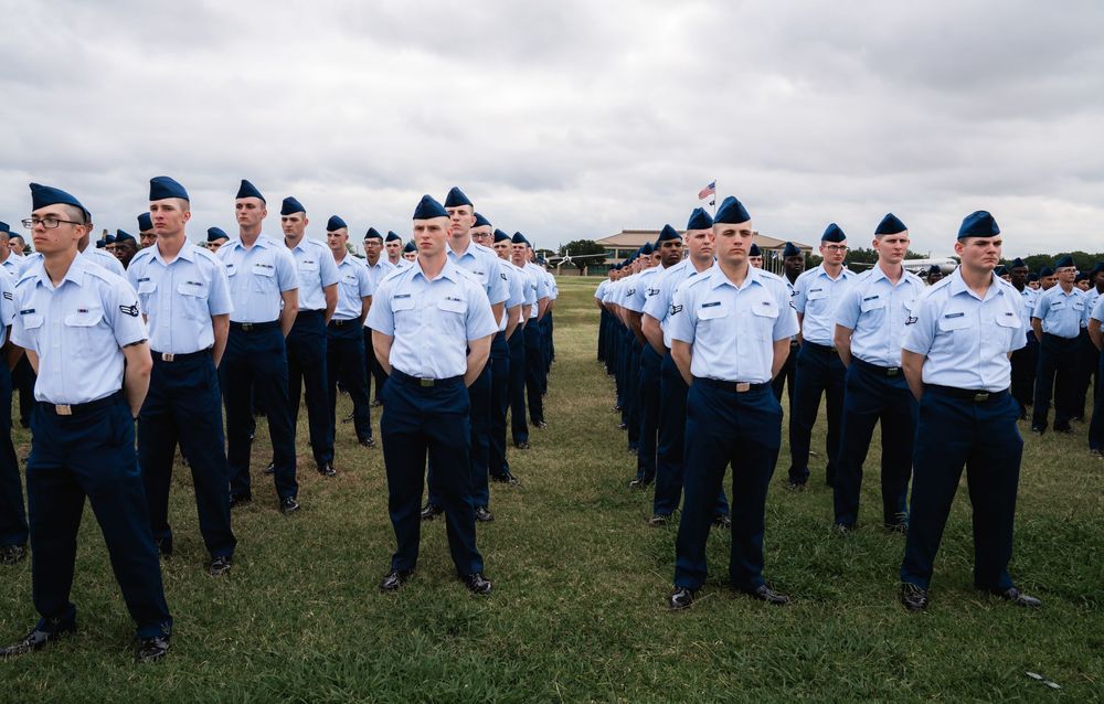 Members of the Air Force stand at attention in formation on a grassy field under cloudy skies.