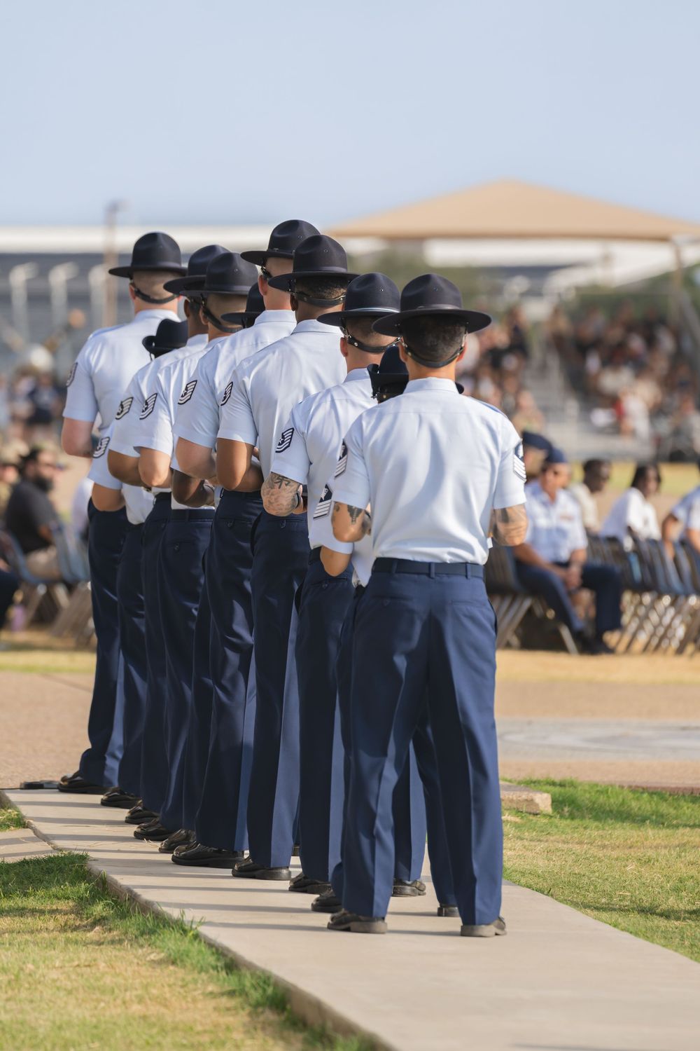 Military personnel in dress uniforms stand at attention in formation during an outdoor ceremony.