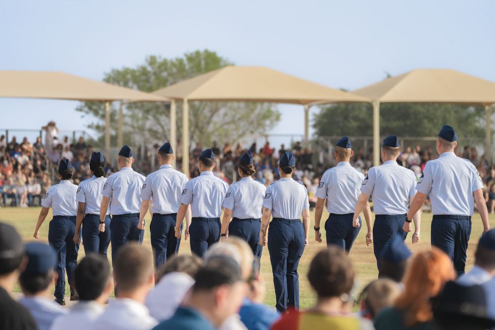 Military personnel stand in a row during an outdoor graduation ceremony with tan canopies overhead.