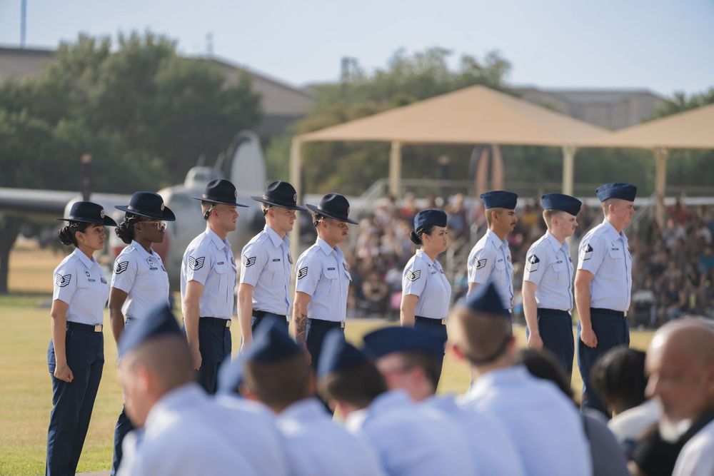 Air Force service members in dress uniforms stand at attention during a formal outdoor ceremony.