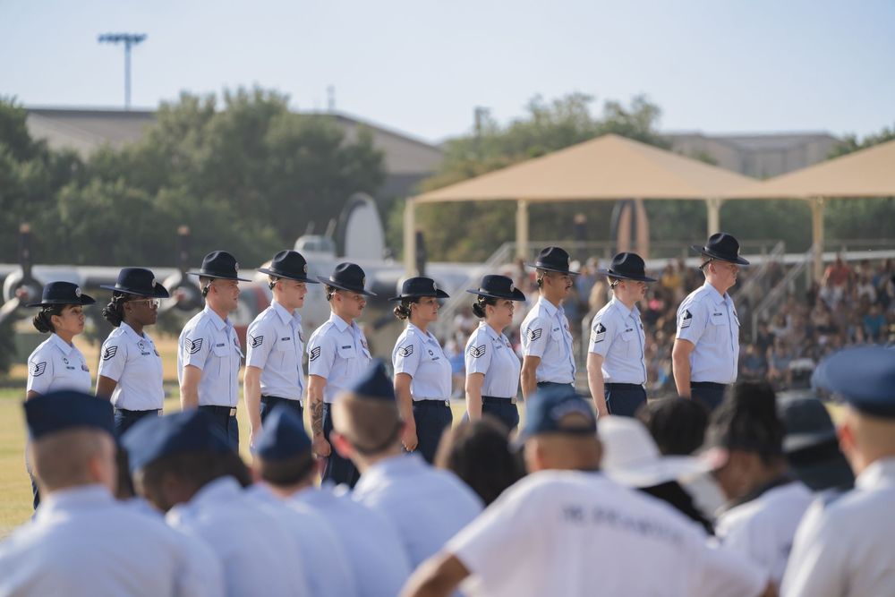 Service members in light blue uniforms and caps stand in formation at an outdoor training facility.