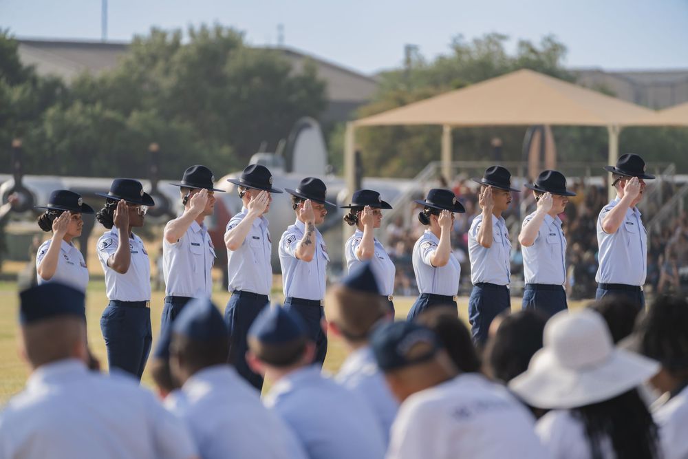 Rows of students line up outdoors in matching white shirts and navy pants during a formal school assembly.