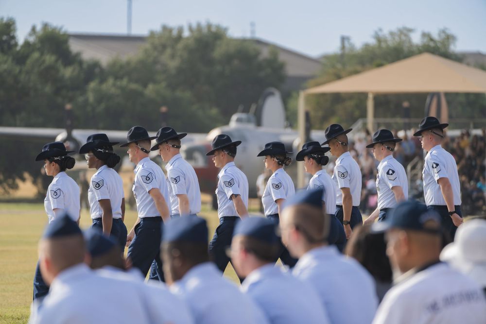 Baseball players wearing black cowboy hats and white jerseys line up during a ceremonial event at a sports field.