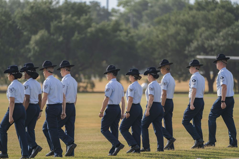 Students wearing navy uniforms stand in formation lines during an outdoor training or ceremony on a grassy field.