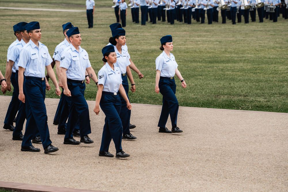 Air Force trainees in blue uniforms march in formation on pathway during military training exercises.