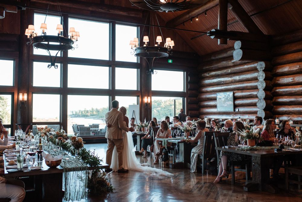 Rustic log cabin wedding reception venue with exposed beams, chandeliers and large windows overlooking scenic views.