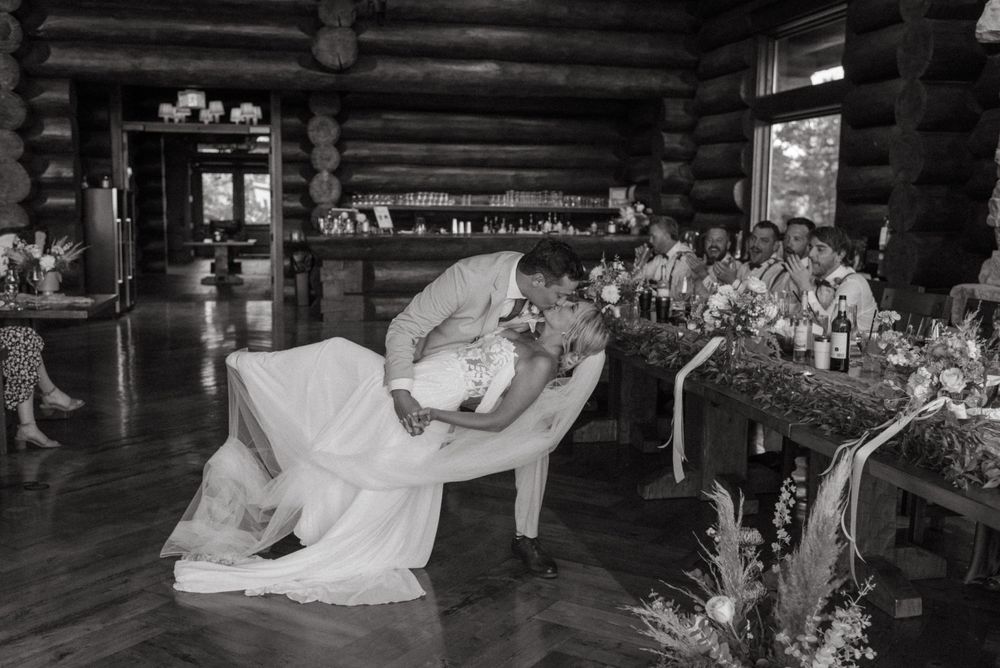 Black and white photo of couple sharing a moment on an antique couch inside a log cabin reception venue.