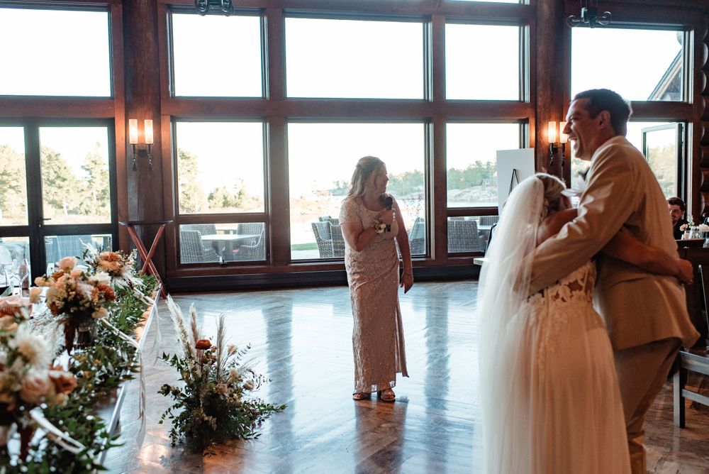 Wedding ceremony at a rustic venue with large windows overlooking natural scenery and floral arrangements.