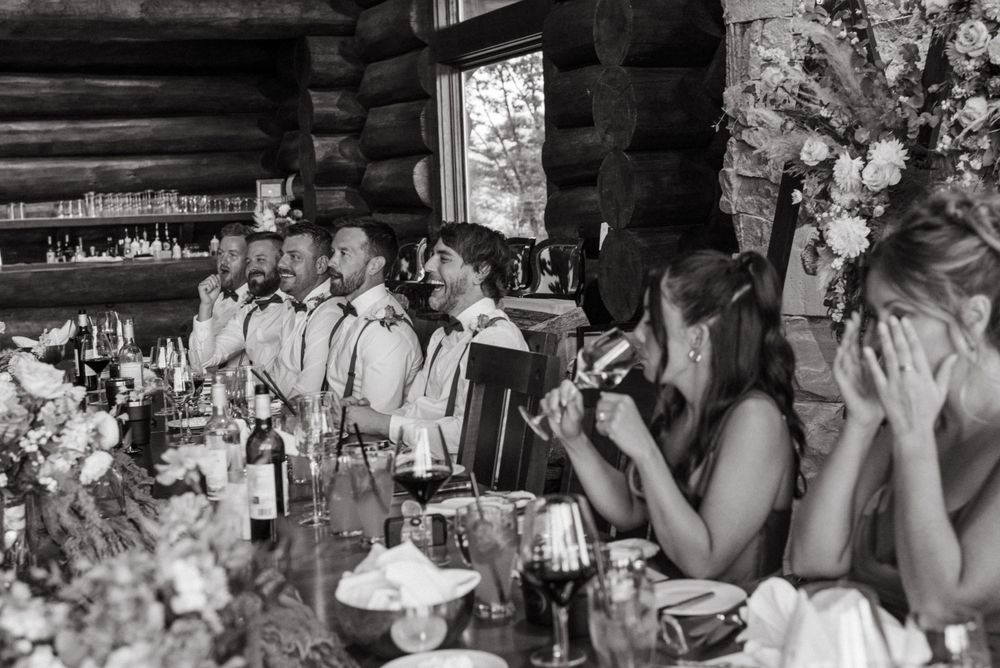 Wedding guests enjoying a festive celebration dinner at a rustic log cabin reception venue with floral decor.